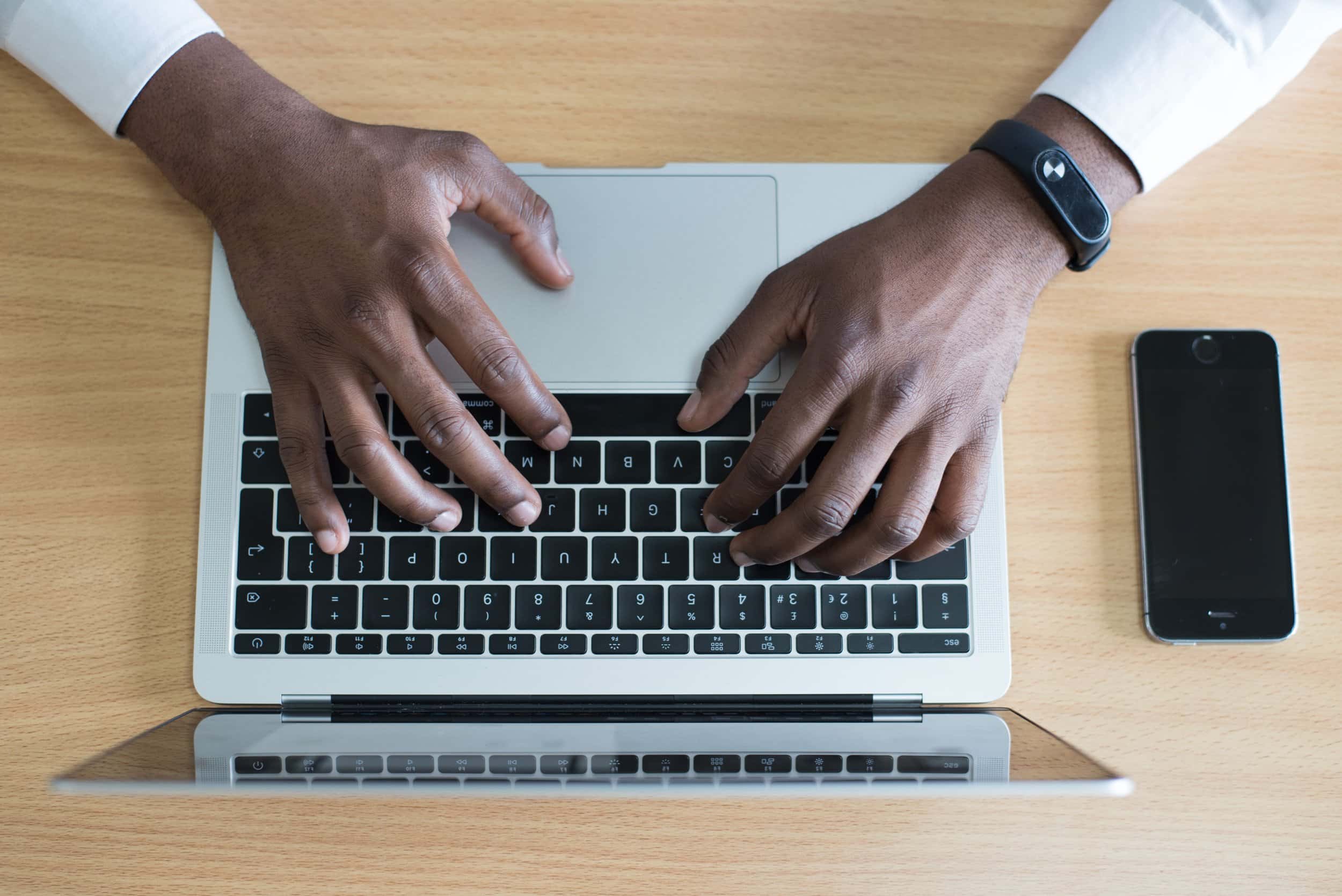man's hands typing on a laptop, which is sitting on a desk