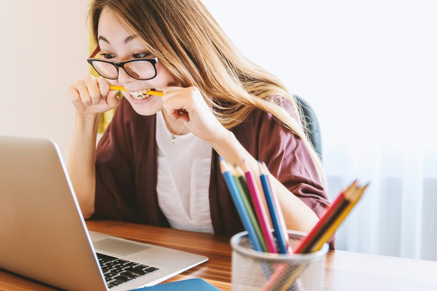 woman looking at laptop screen while biting on a pencil