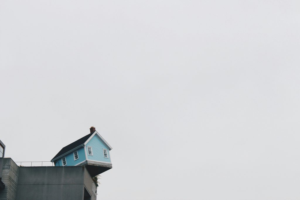 light blue house teetering on edge of high concrete wall