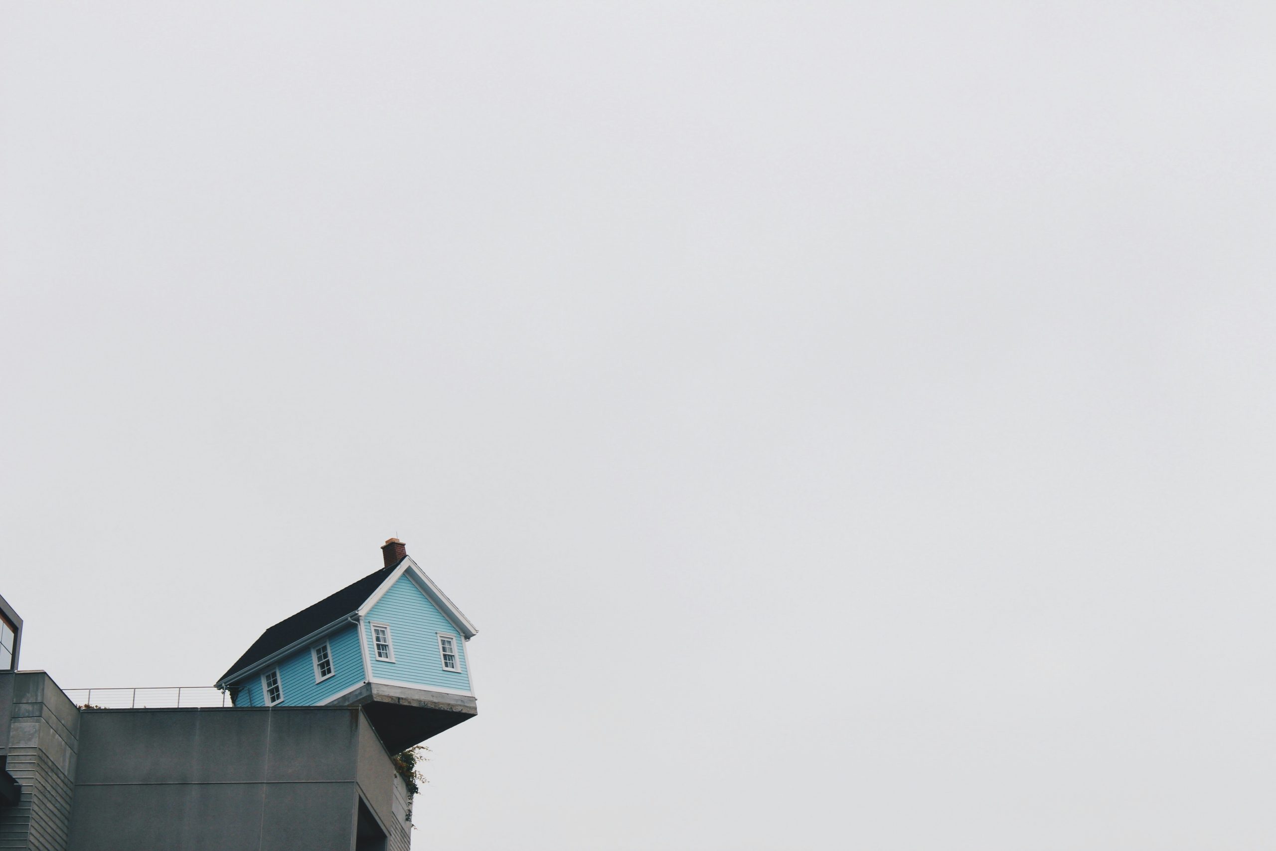 light blue house teetering on edge of high concrete wall