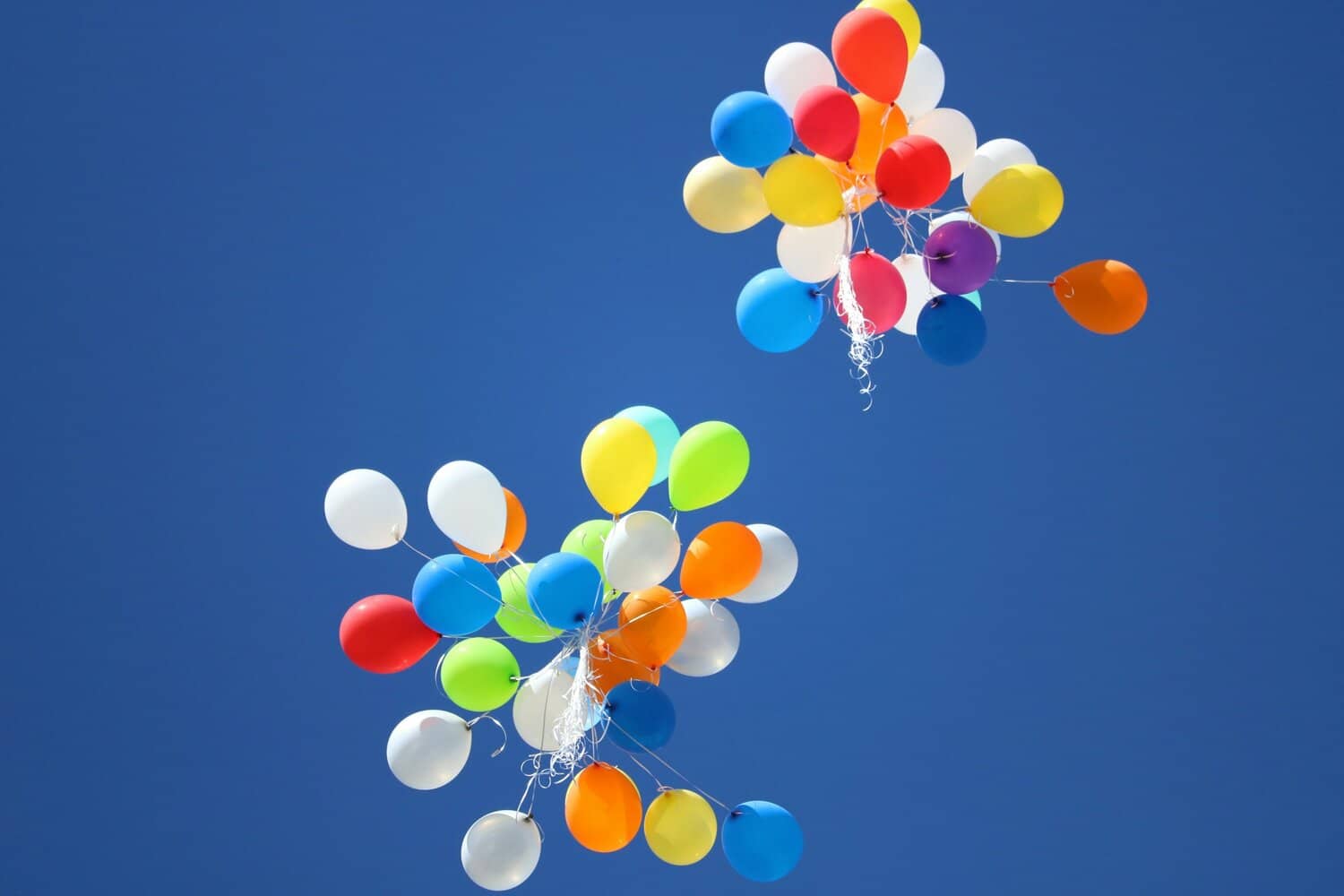 multi-colored balloons floating away into the blue sky