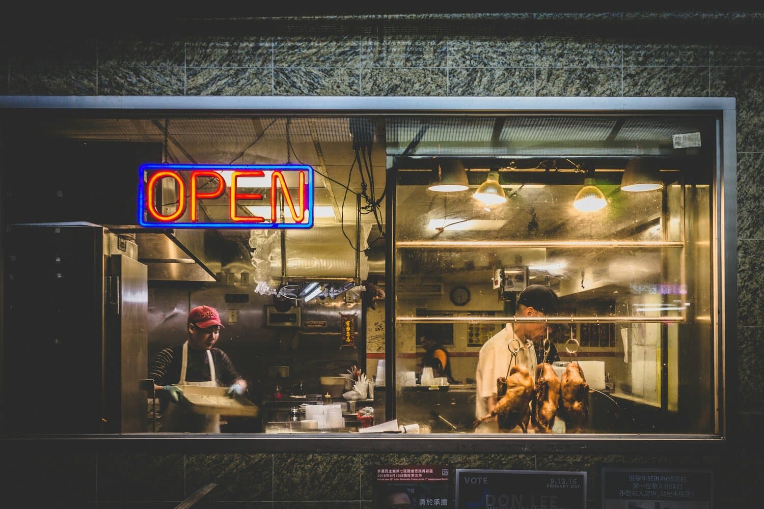 view of restaurant workers through a window with neon open sign