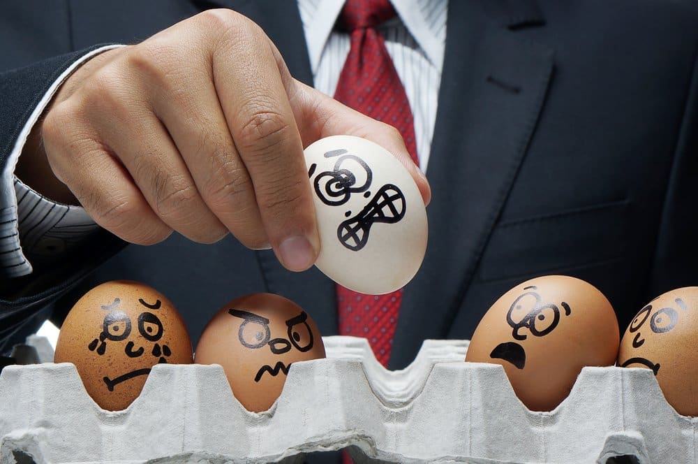 man placing eggs with faces drawn on them into an egg carton