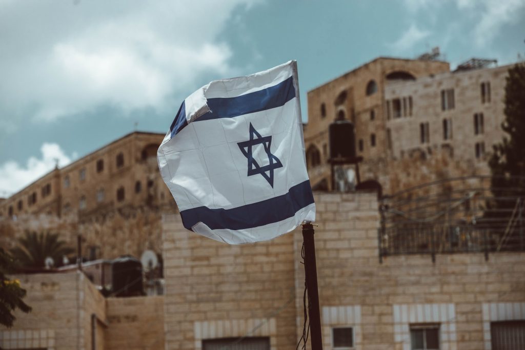 Israel flag in front of stone wall with sky in background