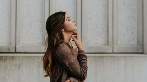 young woman with long brown hair contemplating and thinking in front of a wall