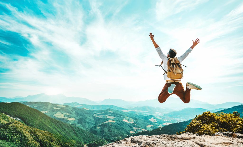 Happy man with backpack jumping on top of the mountain