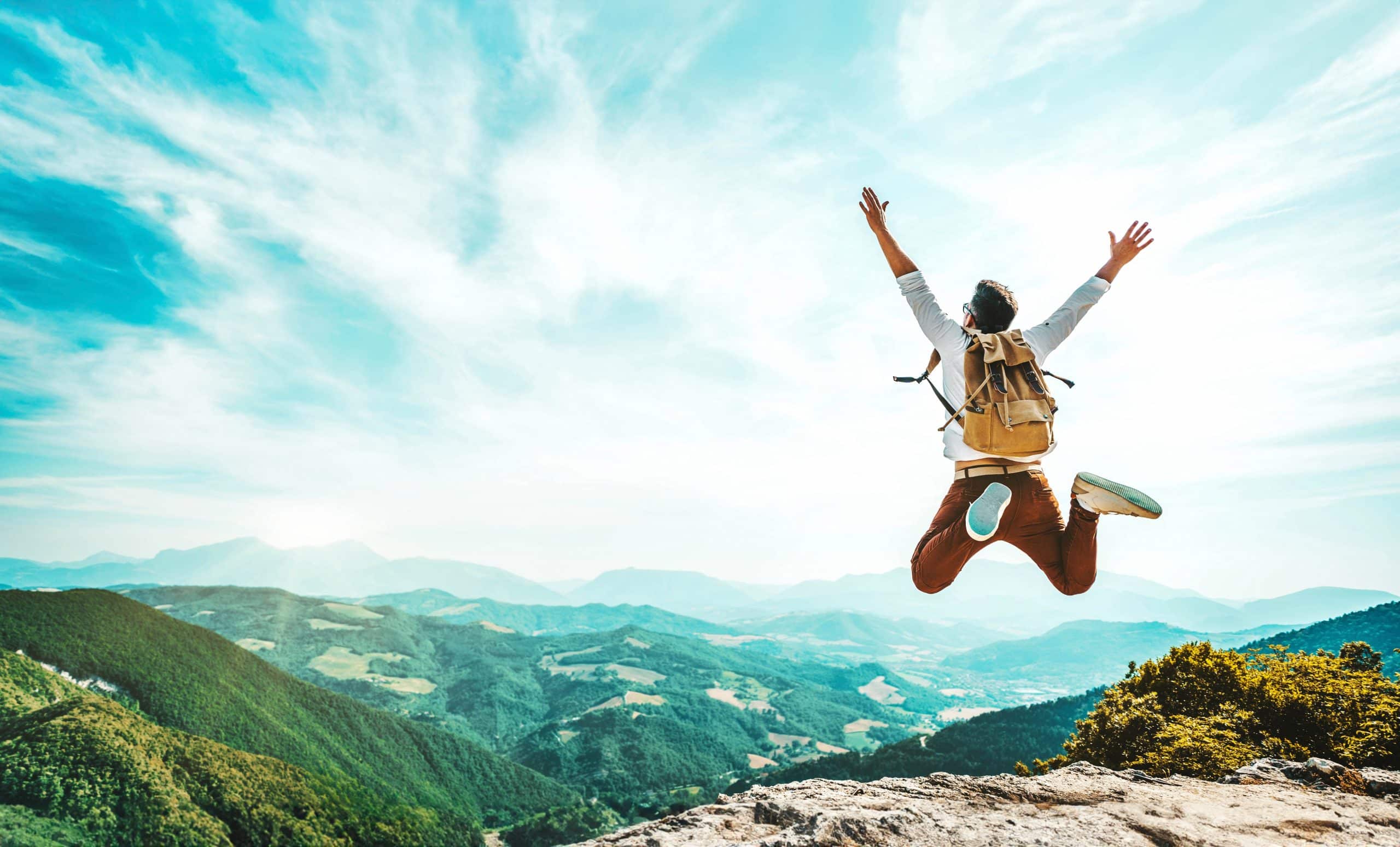 Happy man with backpack jumping on top of the mountain